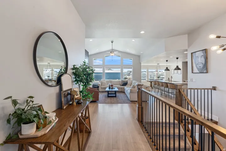 Vaulted ceiling with transom windows, wood-finish flooring, staircase with metal balusters, kitchen island with pendant lighting, and recessed ceiling lights