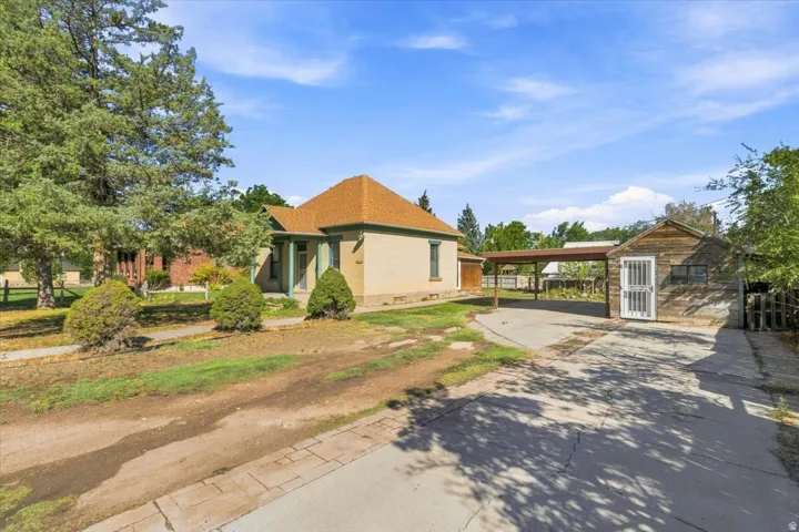 Single-story residence with a covered front porch, a detached wood-sided garage, and an attached carport, all situated on a spacious lot with mature trees