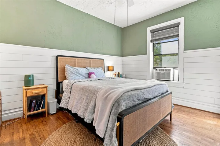 Hardwood flooring, painted walls with shiplap wainscoting, window with blinds, and a ceiling fan