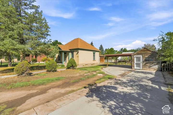 Single-story residence with a covered front porch, a detached wood-sided garage, and an attached carport, all situated on a spacious lot with mature trees