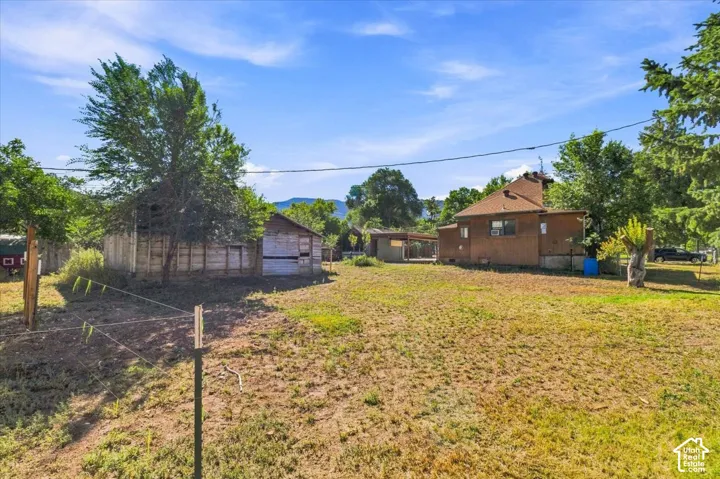 Expansive property featuring a detached outbuilding, mature trees, and a residential structure with a shingle roof