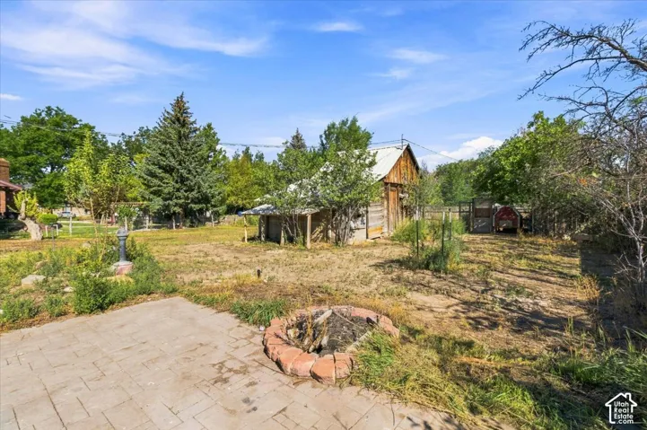 Expansive outdoor space featuring a paved patio, brick-ringed fire pit, and a rustic wood-sided outbuilding
