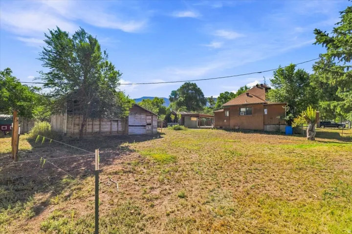 Expansive property featuring a detached outbuilding, mature trees, and a residential structure with a shingle roof
