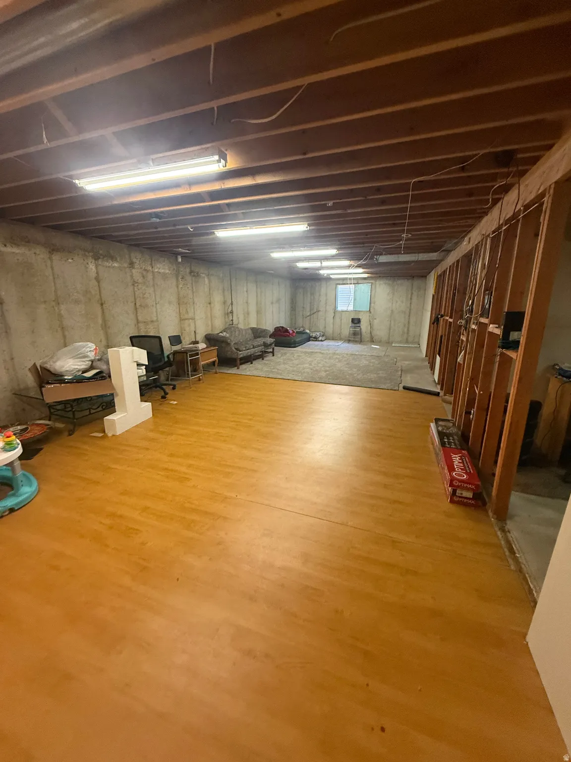 Expansive lower level featuring wood-finish flooring, exposed ceiling joists, concrete walls, and multiple ceiling-mounted light fixtures
