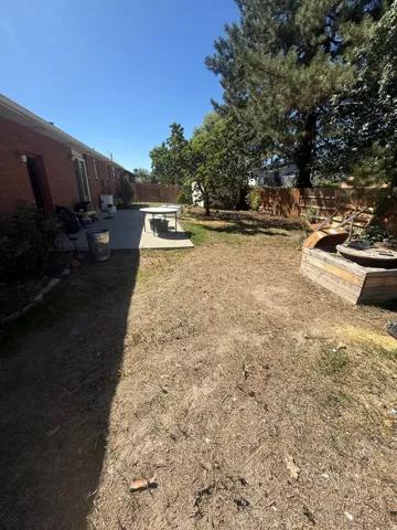 Expansive backyard featuring a concrete patio, mature trees, and a wood privacy fence