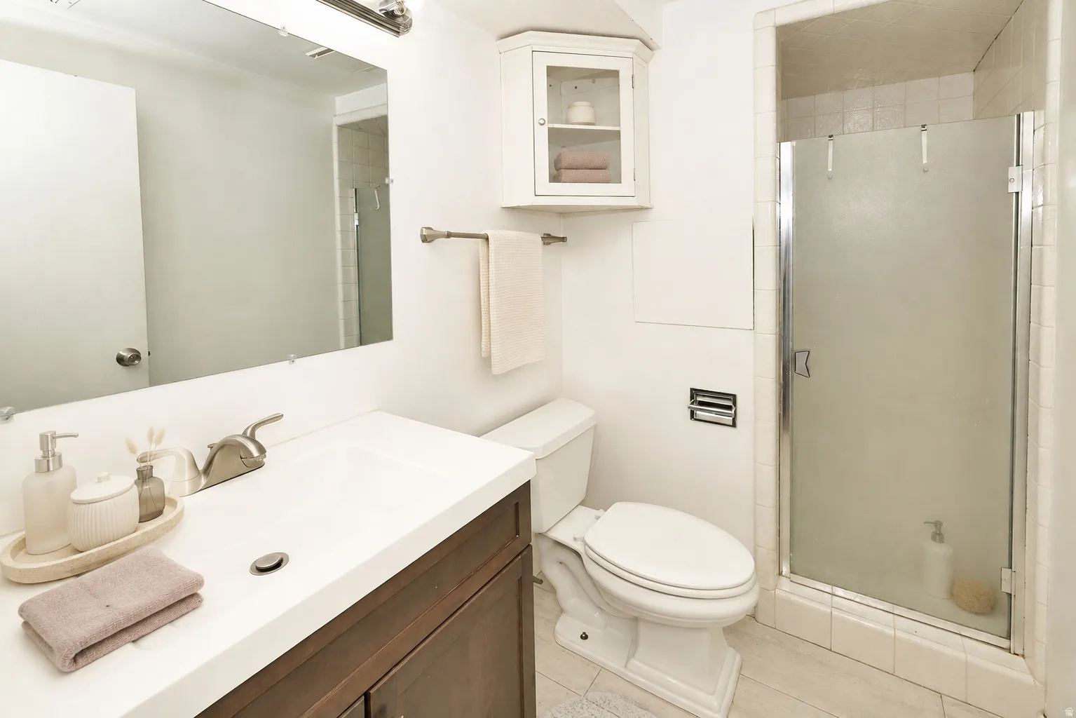 Side B White vanity with integrated sink, brushed nickel faucet, wall-mounted mirror, white wall-mounted corner cabinet, and a glass-enclosed shower