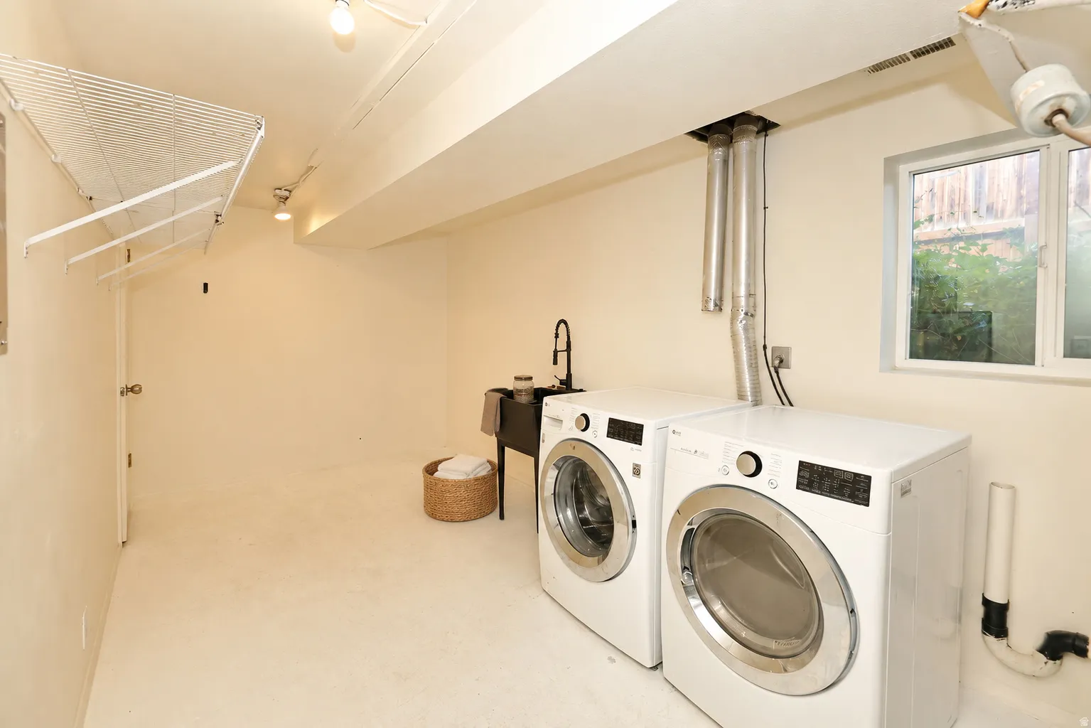Side A Dedicated laundry area featuring a utility sink with a black gooseneck faucet, white front-load appliances, overhead track lighting, and a window for natural illumination
