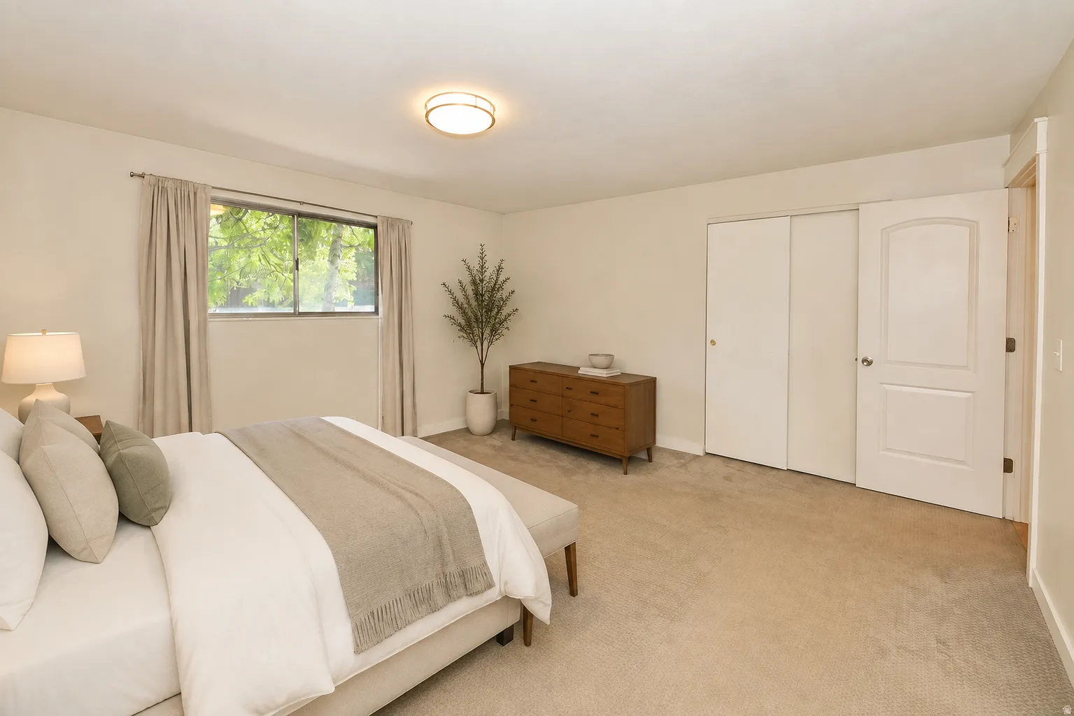 Side A primary bedroom. Recessed window with exterior views, built-in closet with sliding doors, arched panel interior door, and ceiling-mounted light fixture
