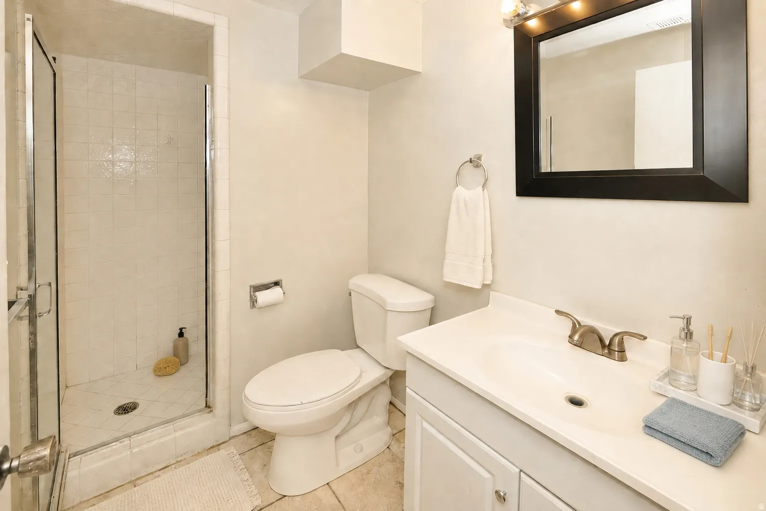 Side A basement bathroom. Tile flooring, glass-enclosed shower, single vanity with integrated sink, dual-handle faucet, and framed mirror with overhead lighting
