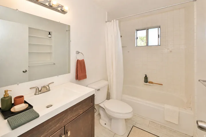 Side B Bathroom featuring a wood-finish vanity with an integrated sink, a full-size mirror, and a bathtub with white subway tile surround