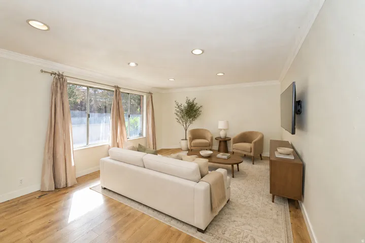 Side A living room. Recessed lighting, crown molding, wood-finish flooring, multiple windows, and a wall-mounted television bracket
