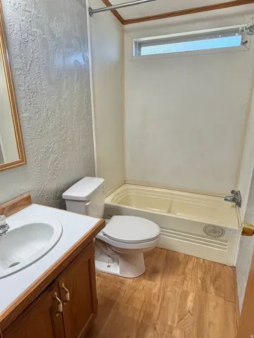 Bathroom with a built-in tub, wood-finish flooring, a wood vanity, and a window