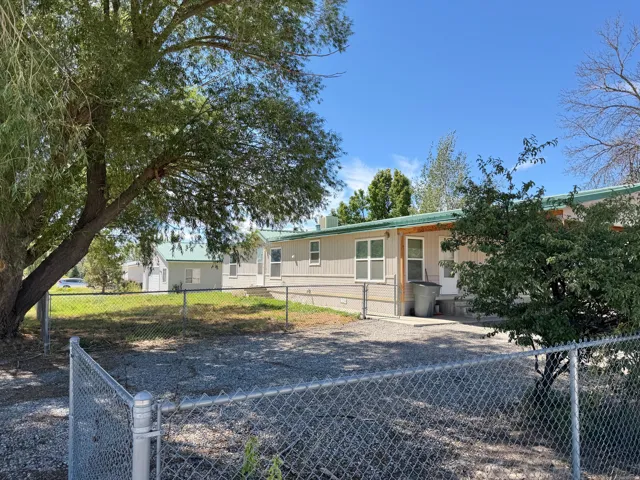 Chain-link perimeter fencing, gravel yard, mature shade trees, and a covered back patio