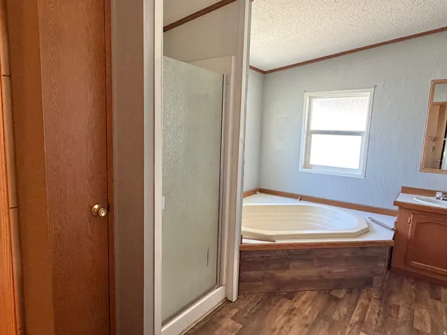 Corner soaking tub, wood-finish flooring, single vanity with integrated sink, framed mirror, and a window