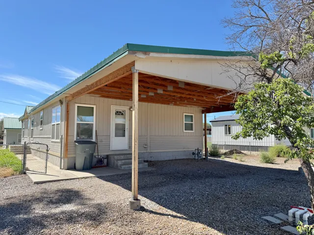 Covered parking structure, gravel driveway, chain-link fence, exterior siding, and a green metal roof