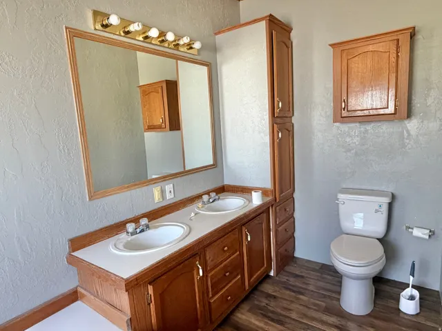 Dual vanity with integrated sinks and wood-finish cabinetry, a large framed mirror, and a brass-tone light fixture