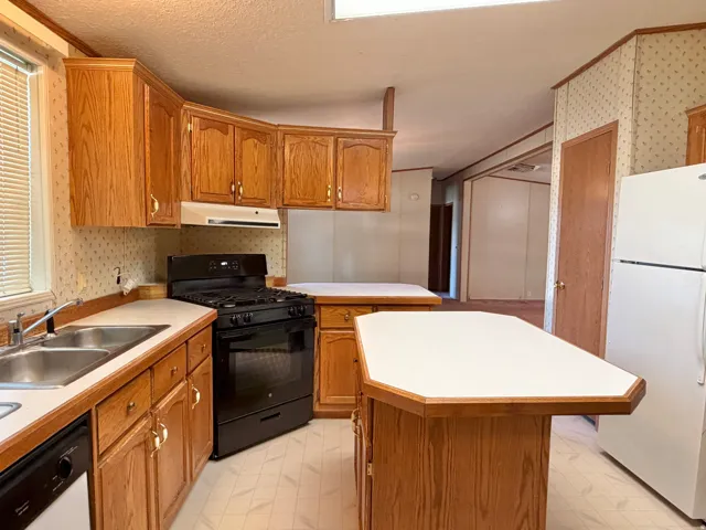 Kitchen featuring wood cabinetry, a black gas range, a double basin sink, and a center island with counter seating