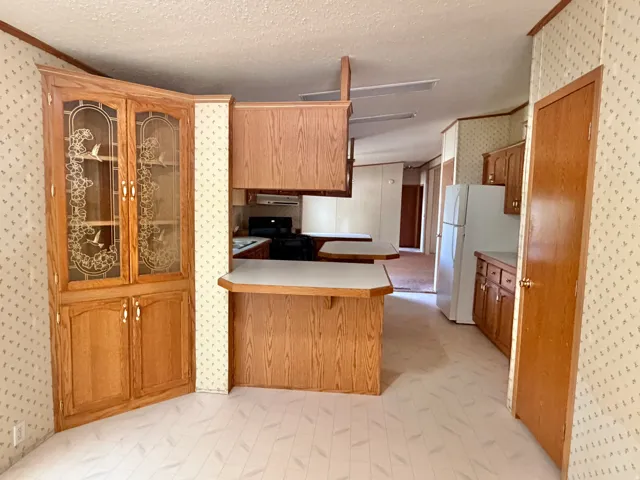Kitchen featuring wood-finish cabinetry, built-in corner display cabinet with glass-front doors, white appliances, and a peninsula counter with breakfast bar seating