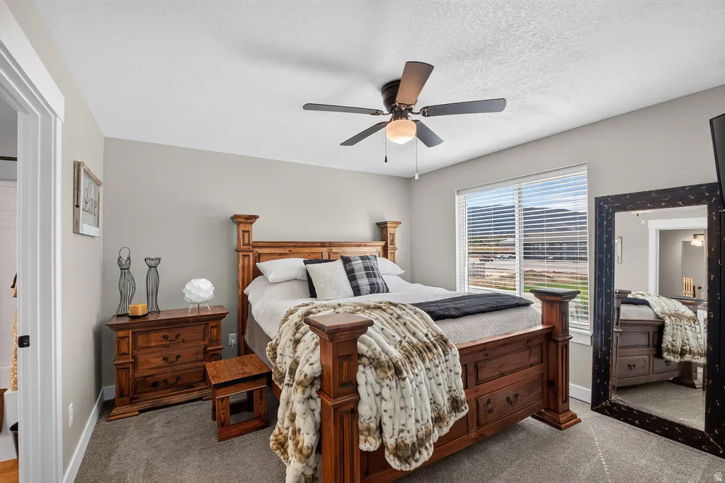 Carpeted bedroom featuring a window with blinds, ceiling fan with light fixture, and light-colored wall paint