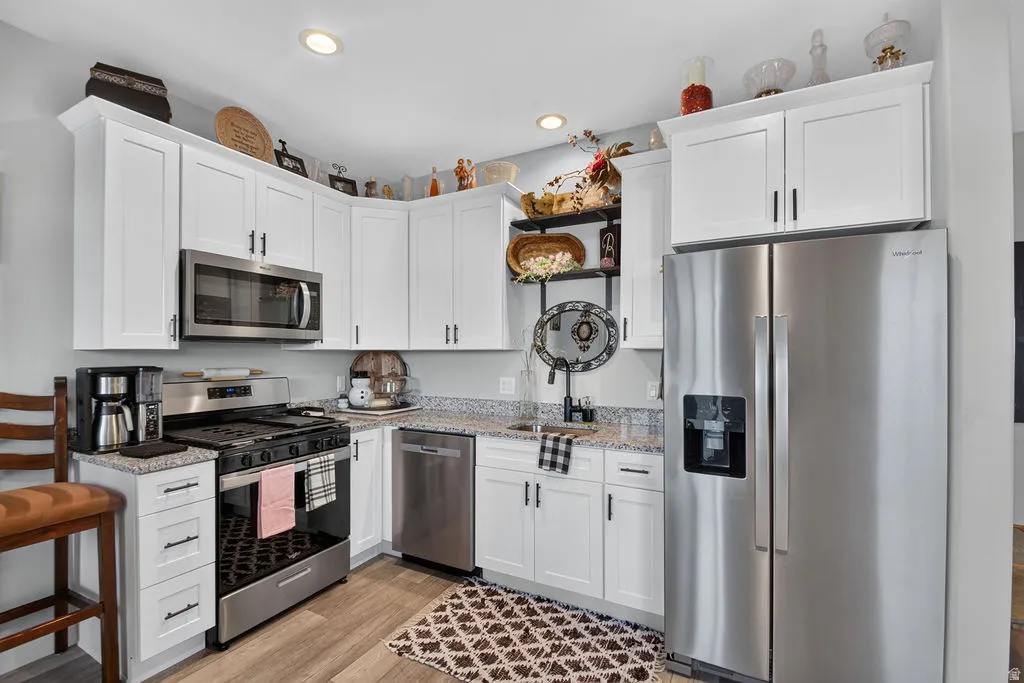 White shaker-style cabinetry, stainless steel appliances, granite countertops, wood-finish flooring, and recessed lighting