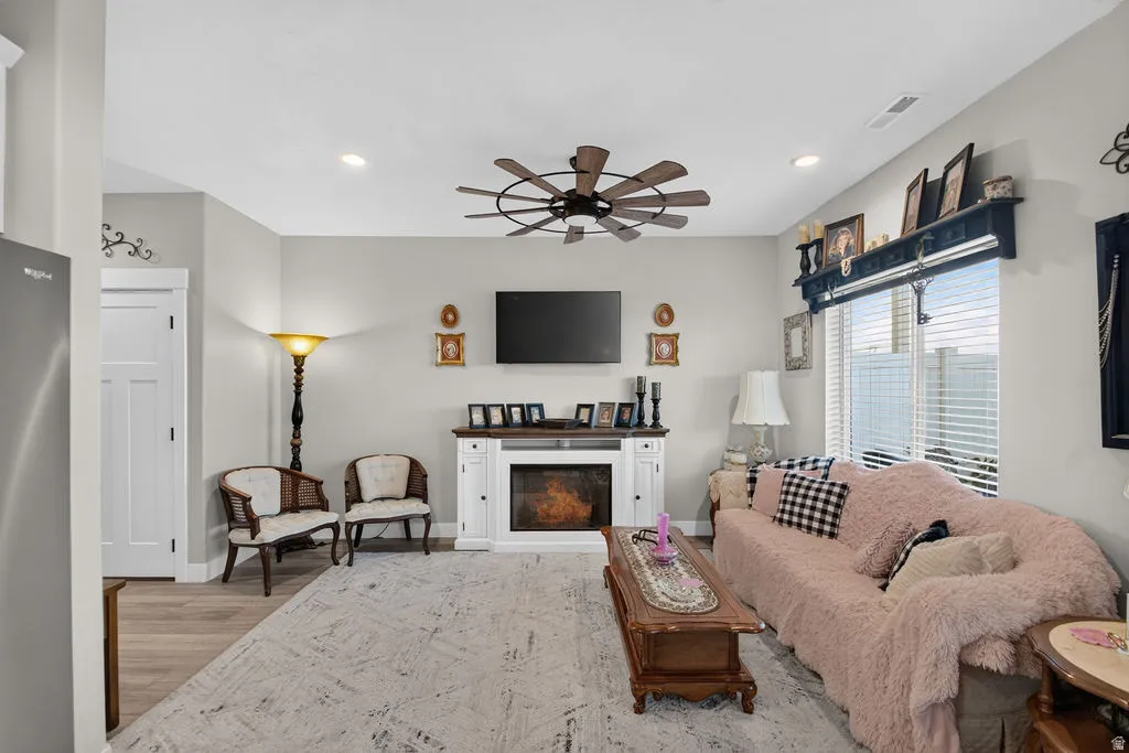 Living area featuring an electric fireplace with a white mantel, wood-finish flooring, recessed lighting, and a ceiling fan