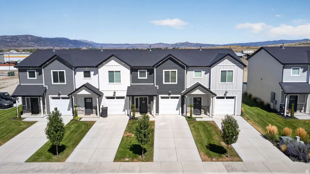 Modern townhome exteriors featuring vertical and horizontal siding, dark roofs, individual driveways, and manicured landscaping