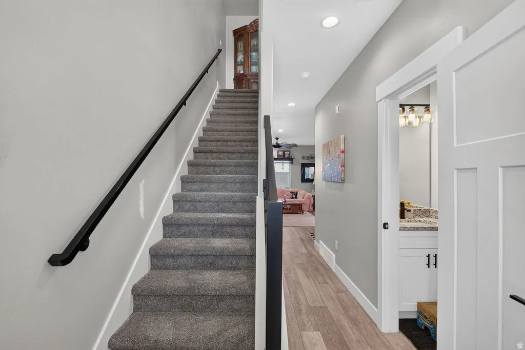 Carpeted staircase with a black metal handrail, wood-finish flooring, recessed lighting, and a bathroom vanity with a stone countertop