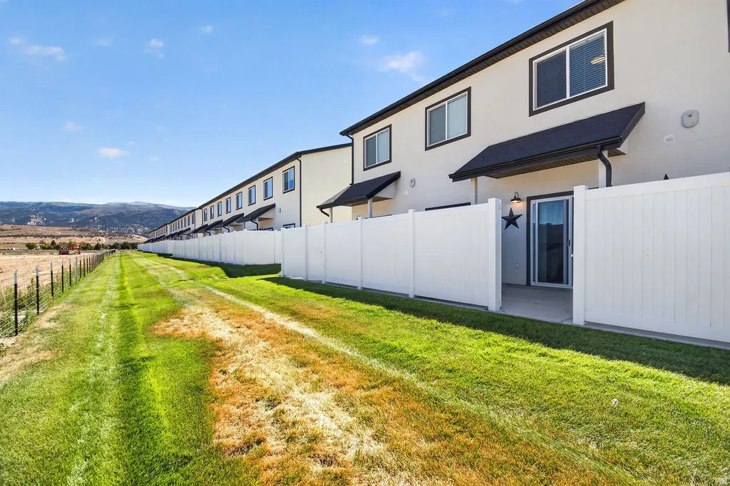 Rear exterior featuring a sliding glass door, private patio, white privacy fencing, and a manicured lawn leading to open land
