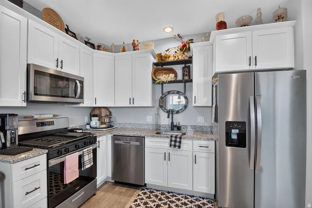 White cabinetry with dark hardware, stainless steel appliances, speckled stone countertops, and wood-finish flooring
