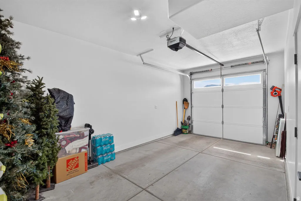 Concrete flooring, white painted walls, overhead lighting, automatic garage door opener, garage door with upper window panes