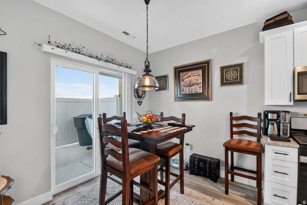 Sliding glass door, light wood-finish flooring, white cabinetry, dark countertop, and pendant lighting