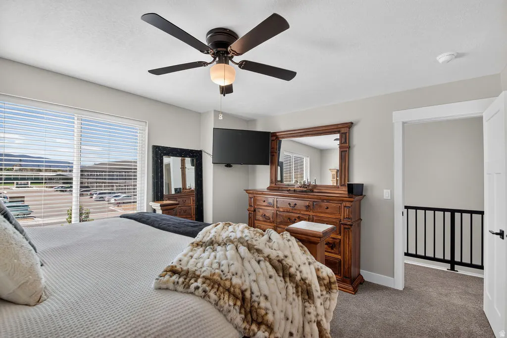 Spacious bedroom featuring light neutral wall tones, a ceiling fan with integrated lighting, and a large window with horizontal blinds