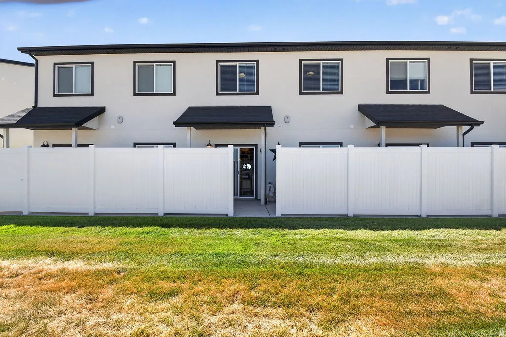 White privacy fencing enclosing a concrete patio area, featuring dark awnings over rear entries