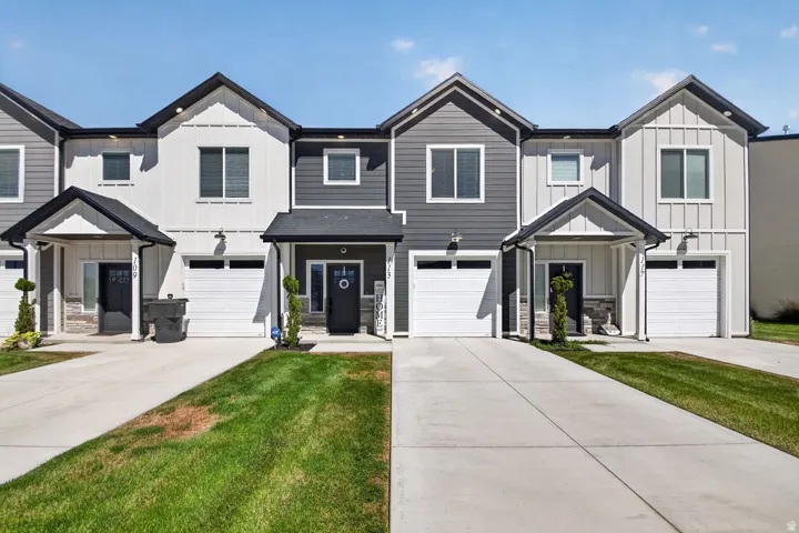 Modern townhome exterior featuring a combination of horizontal and vertical siding, covered entryways, attached garages, and a paved driveway