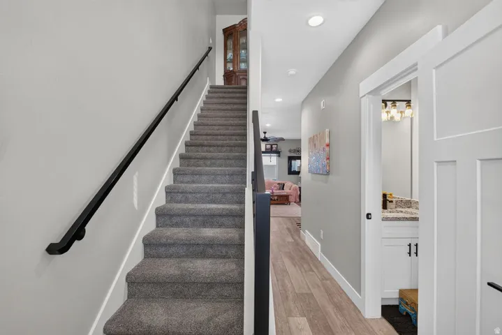 Carpeted staircase with a black metal handrail, wood-finish flooring, recessed lighting, and a bathroom vanity with a stone countertop