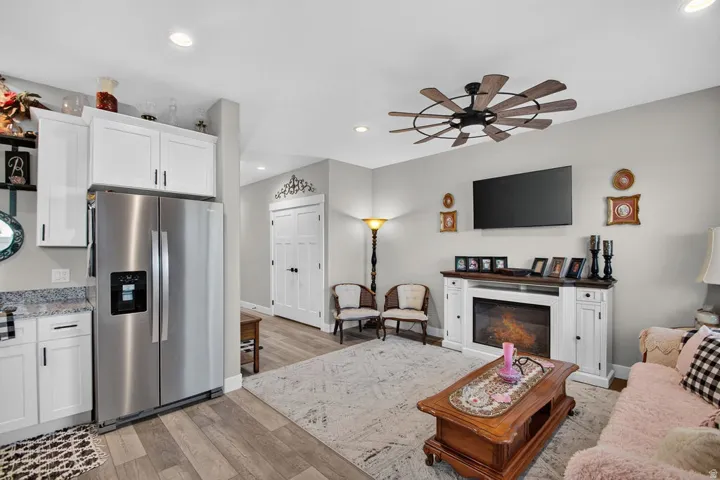 Stainless steel refrigerator, white cabinetry, wood-finish flooring, recessed lighting, and a ceiling fan with wood-look blades