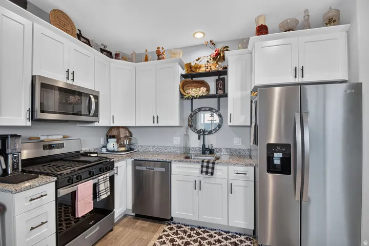 White cabinetry with dark hardware, stainless steel appliances, speckled stone countertops, and wood-finish flooring