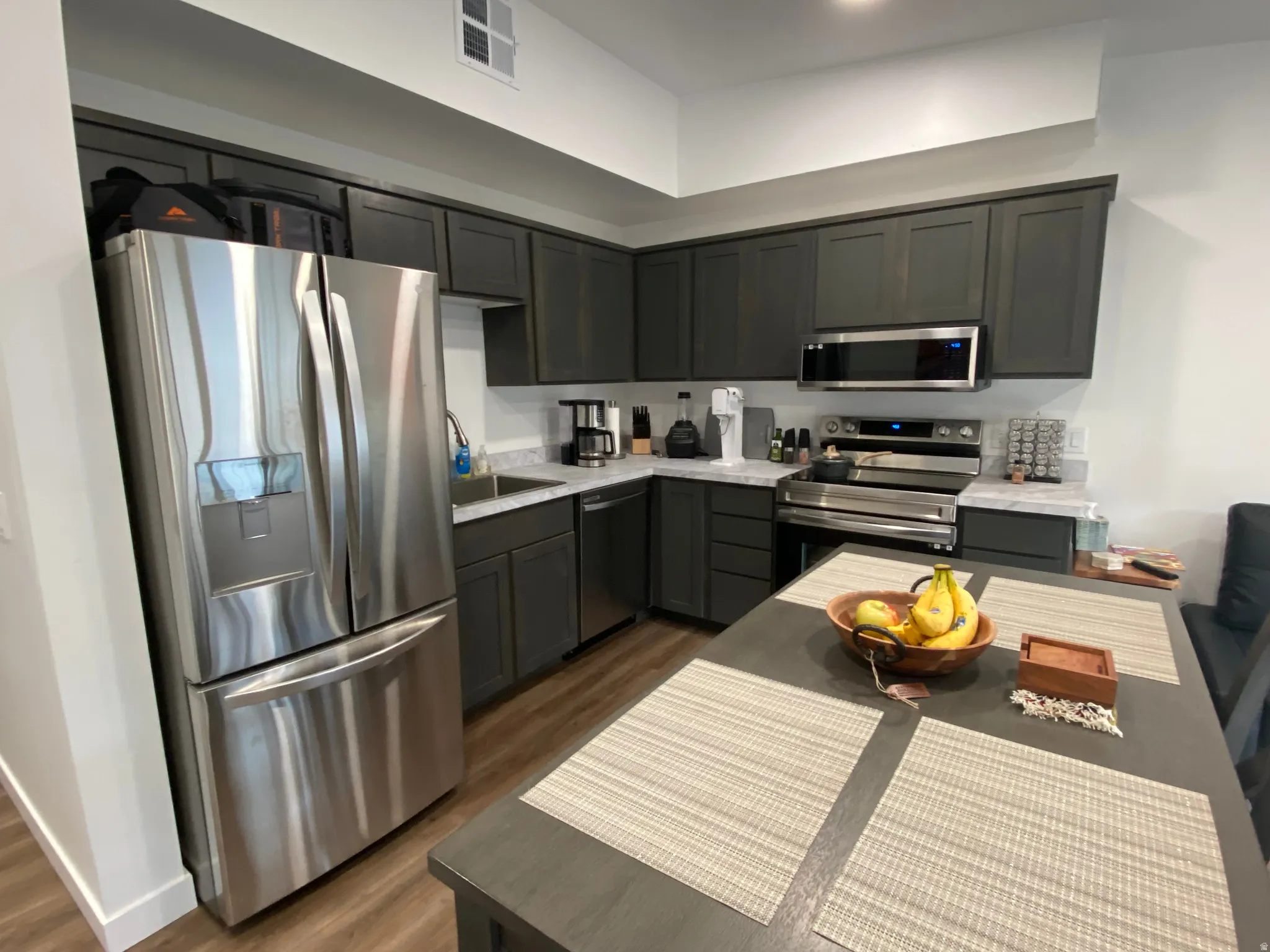 Kitchen featuring stainless steel appliances, dark cabinetry, light countertops, and wood-finish flooring