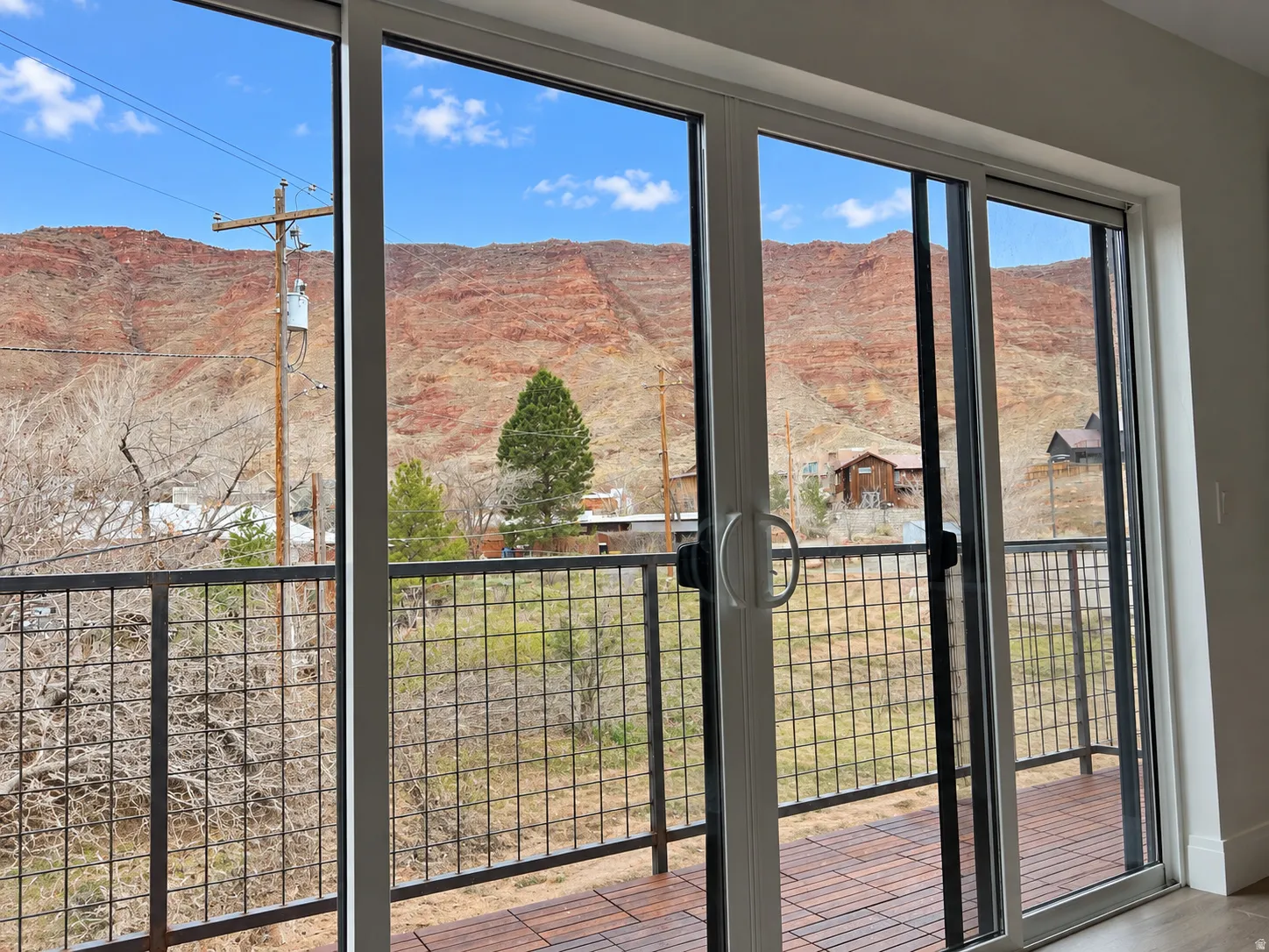 Sliding glass doors with white framing, opening to a balcony with black grid railing and wood-finish decking