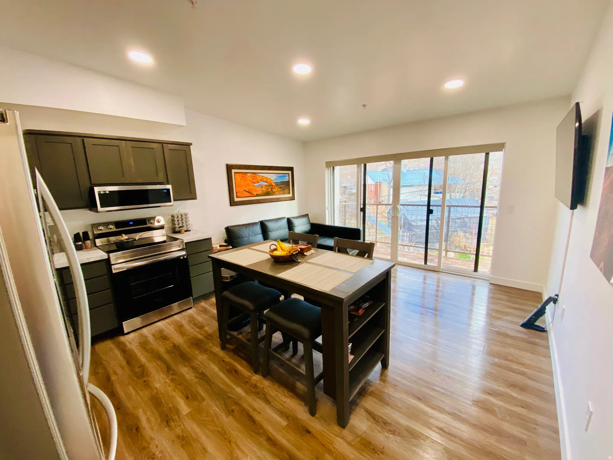 Recessed lighting, wood-finish flooring, dark-toned cabinetry, stainless steel appliances, and sliding glass doors