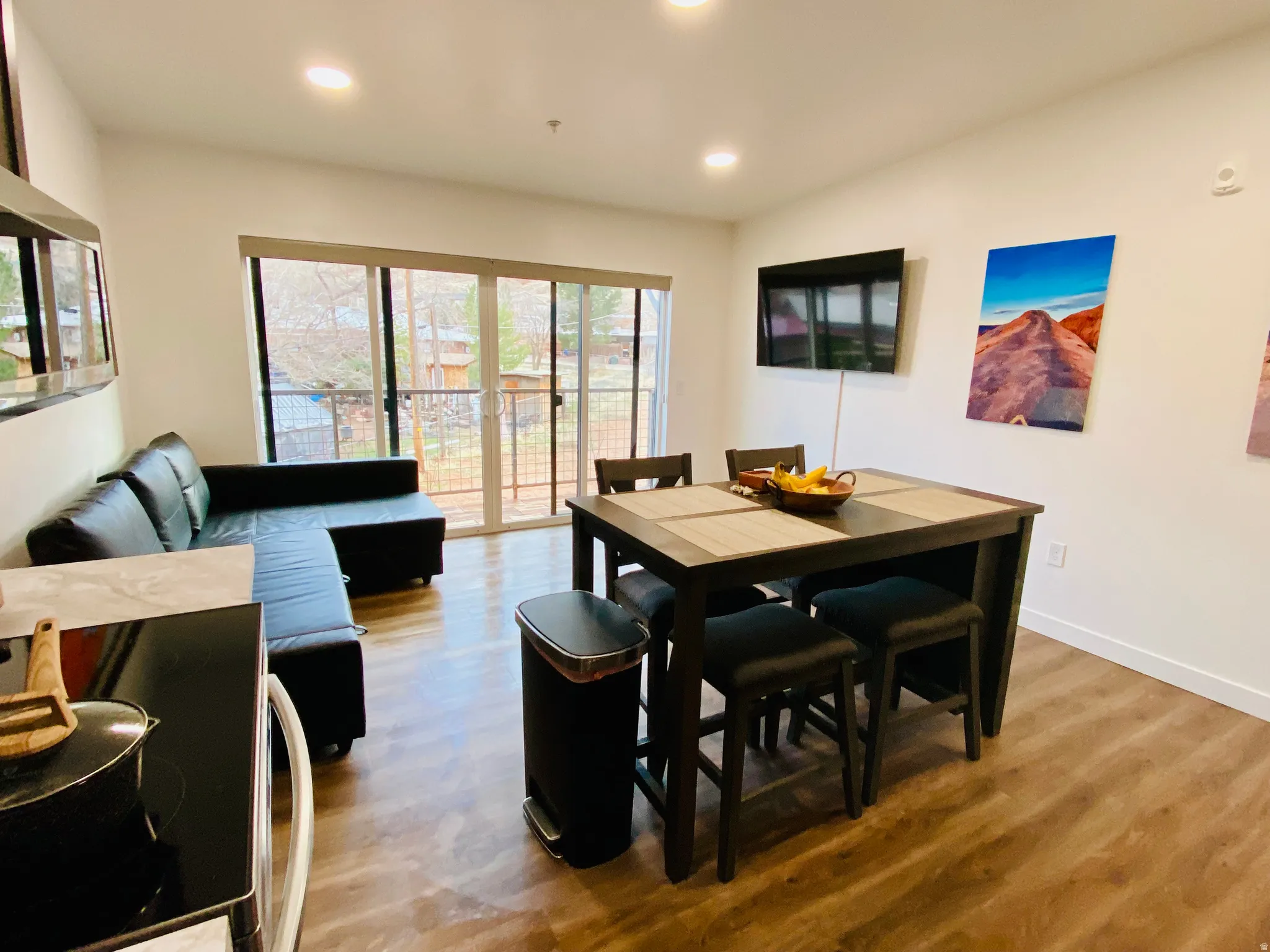 Open-concept living space with wood-finish flooring, recessed lighting, and a sliding glass door leading to an outdoor balcony