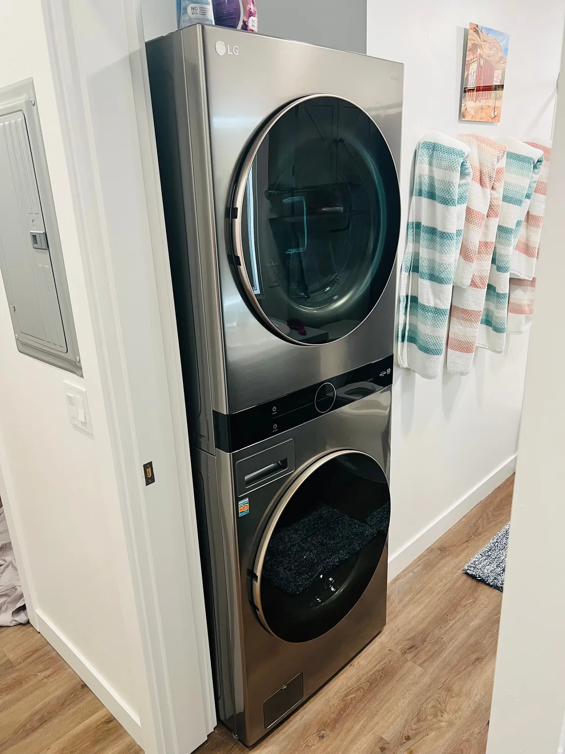 Stacked laundry unit with front-loading appliance, brushed metal finish, and wood-finish flooring