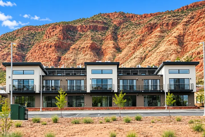 Contemporary exterior with flat rooflines, multiple balconies with glass railings, large glass doors, and a backdrop of expansive red rock formations