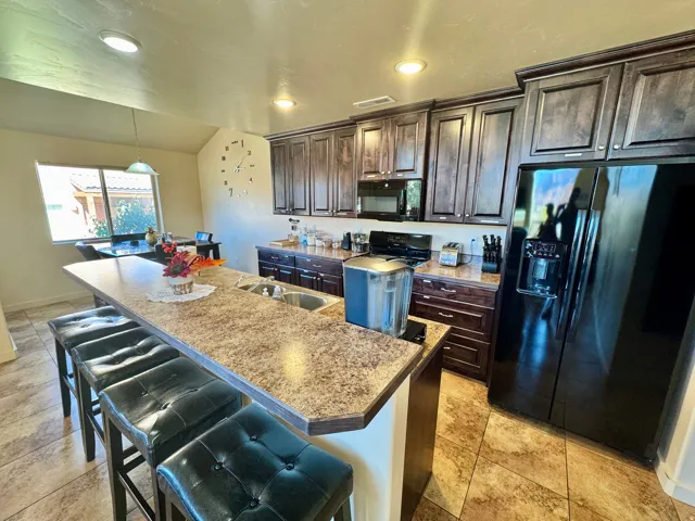Kitchen featuring an extended island with a double sink, dark wood cabinetry, black appliances, and tiled flooring