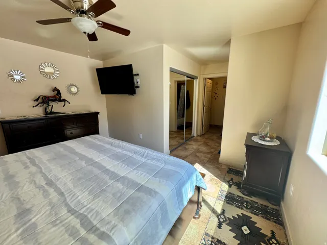 Ceiling fan with integrated lighting, wall-mounted television bracket, mirrored closet doors, and tile flooring