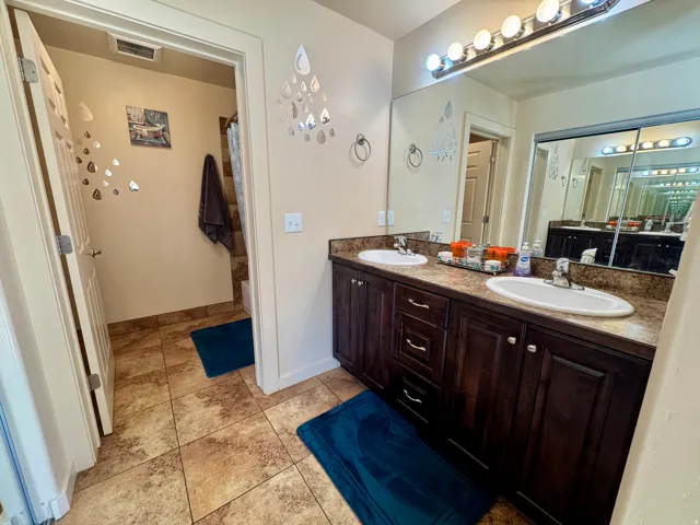 Dual vanity with integrated sinks, dark wood-finish cabinetry, a full-width mirror, and tile flooring