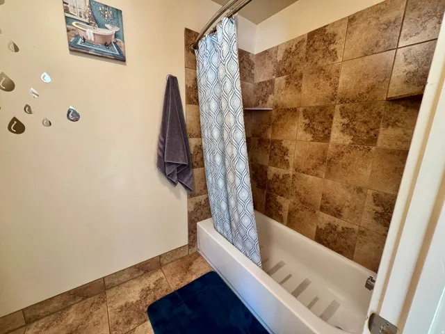 Bathtub with a curved shower rod, brown tiled shower surround, and integrated shower shelf
