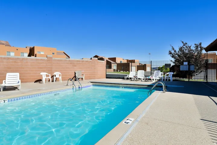 In-ground swimming pool with a concrete surround, featuring a metal entry ladder and perimeter fencing