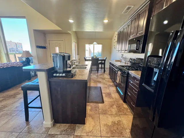 Open-concept kitchen with dark wood-finish cabinetry, black appliances, and a breakfast bar