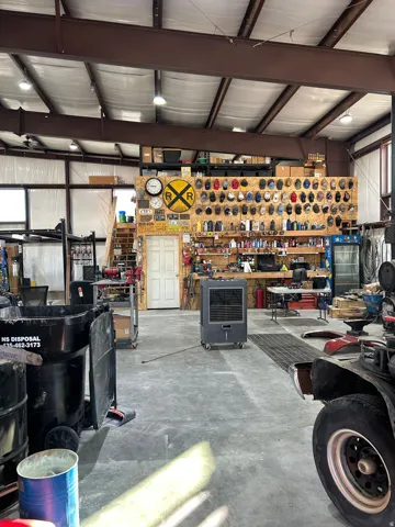 Large workshop space featuring concrete flooring, exposed metal ceiling beams, and integrated lighting fixtures